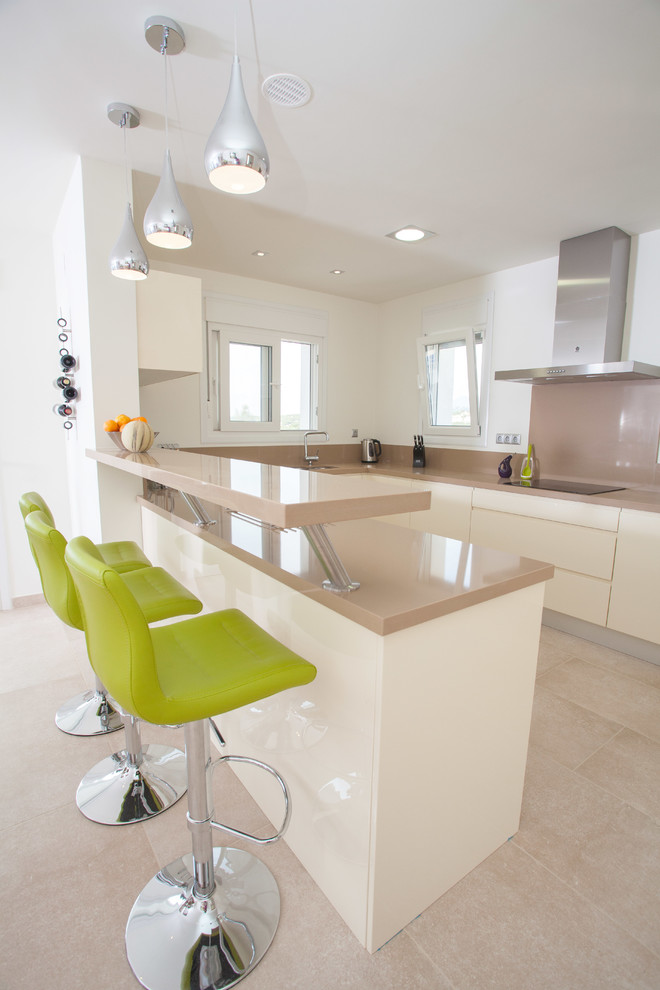 Photo of a mid-sized contemporary u-shaped eat-in kitchen in Alicante-Costa Blanca with flat-panel cabinets, white cabinets, beige splashback, a peninsula, solid surface benchtops, ceramic splashback, stainless steel appliances, limestone floors and beige floor.