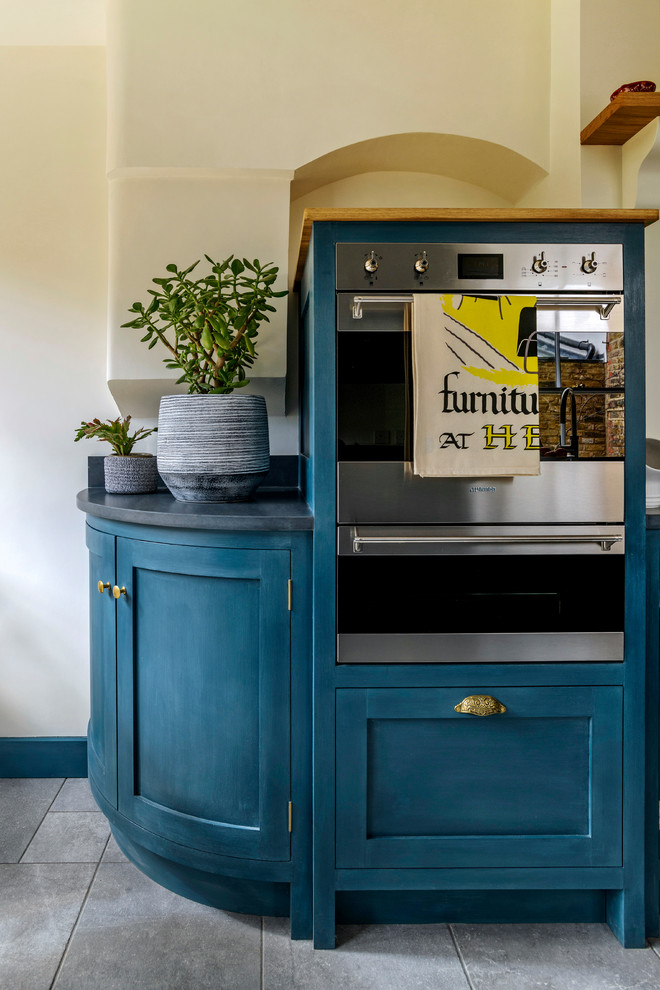 Inspiration for a traditional kitchen in London with a farmhouse sink, shaker cabinets, blue cabinets, granite benchtops, yellow splashback, glass sheet splashback, ceramic floors and black benchtop.