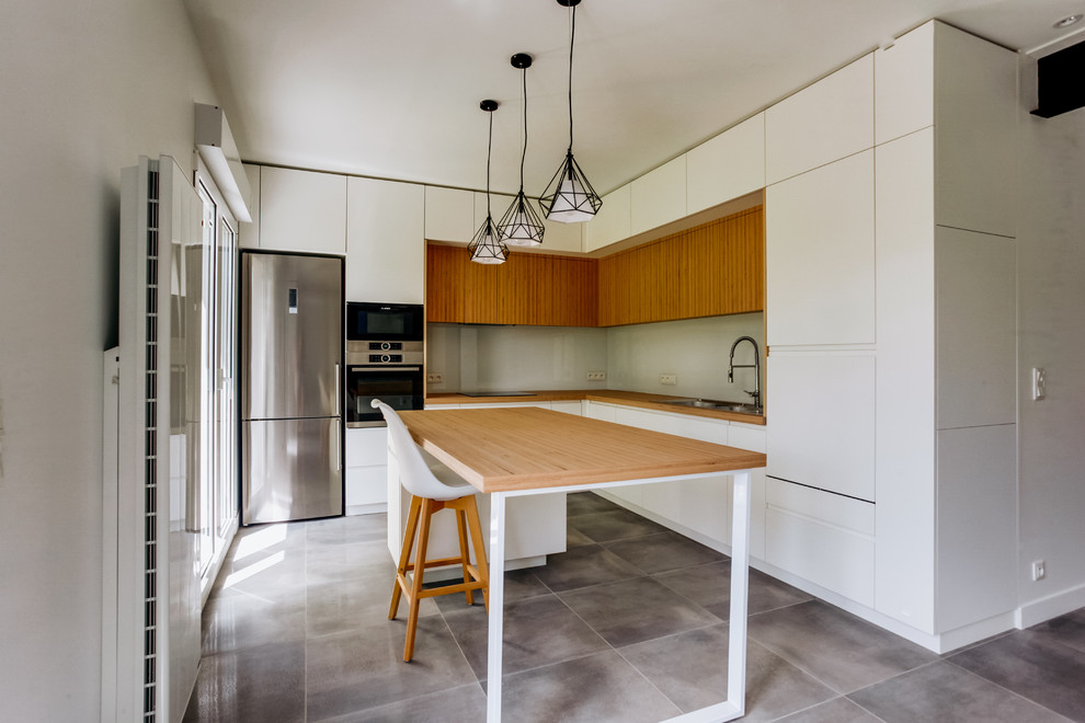 Contemporary galley eat-in kitchen in Paris with a drop-in sink, flat-panel cabinets, white cabinets, wood benchtops, beige splashback, glass sheet splashback, stainless steel appliances, with island, grey floor and brown benchtop.