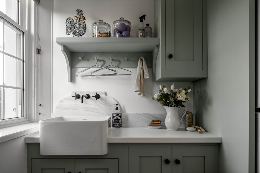 Foto på en liten vita linjär tvättstuga enbart för tvätt, med en rustik diskho, luckor med infälld panel, blå skåp, marmorbänkskiva, vitt stänkskydd, stänkskydd i marmor, vita väggar, ljust trägolv, en tvättpelare och brunt golv