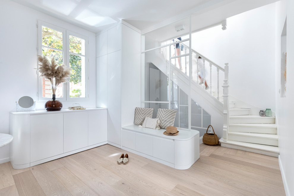 Example of a large light wood floor foyer design in Paris with white walls