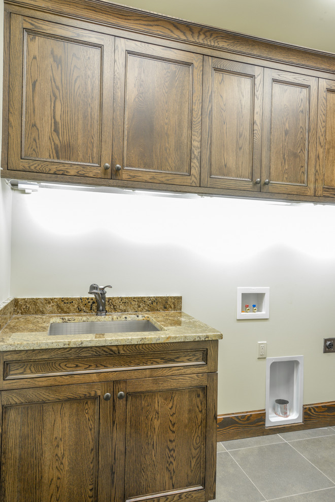 Mid-sized mountain style single-wall slate floor and gray floor dedicated laundry room photo with an undermount sink, recessed-panel cabinets, dark wood cabinets, granite countertops, white walls, a side-by-side washer/dryer and brown countertops
