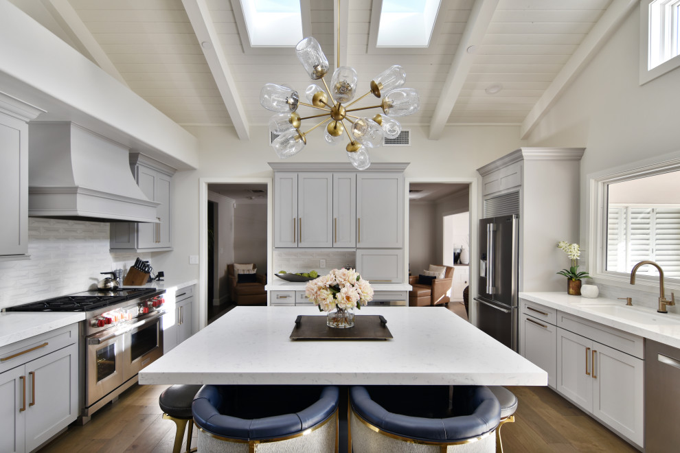 Inspiration for a transitional u-shaped medium tone wood floor, brown floor, exposed beam, shiplap ceiling and vaulted ceiling kitchen remodel in Phoenix with an undermount sink, shaker cabinets, white cabinets, white backsplash, stainless steel appliances, an island and white countertops