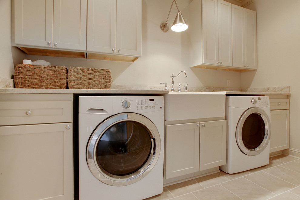 This is an example of a large traditional single-wall utility room in New Orleans with a farmhouse sink, shaker cabinets, white cabinets, quartzite benchtops, white walls and ceramic floors.