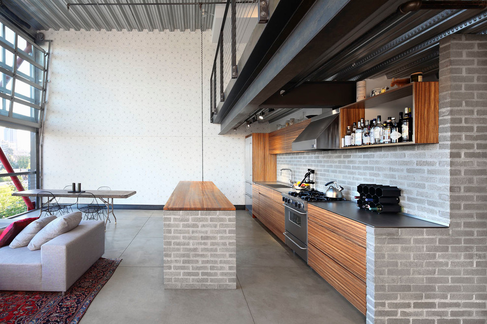 Inspiration for a small industrial galley open plan kitchen in Seattle with an undermount sink, flat-panel cabinets, light wood cabinets, wood benchtops, grey splashback, brick splashback, stainless steel appliances, concrete floors, with island and grey floor.