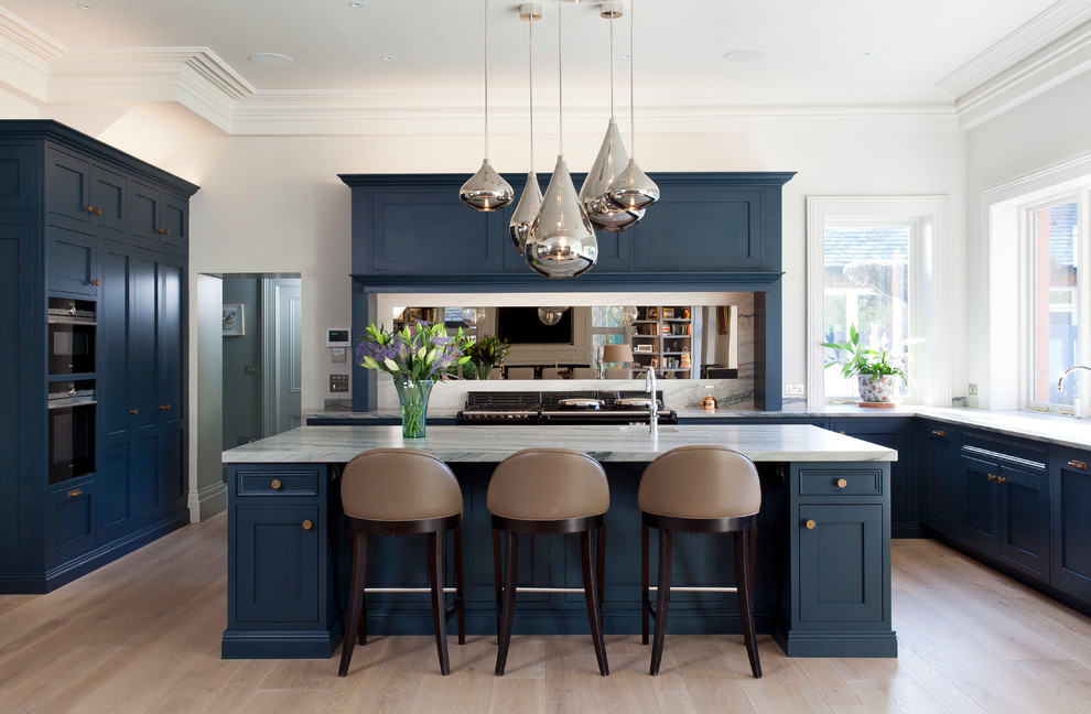 Photo of a transitional u-shaped eat-in kitchen in Cheshire with beaded inset cabinets, marble benchtops, mirror splashback, light hardwood floors, with island, white benchtop, blue cabinets, black appliances and beige floor.