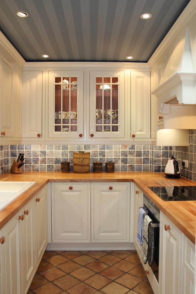 Inspiration for a small traditional u-shaped kitchen in Other with raised-panel cabinets, white cabinets, wood benchtops, blue splashback, stone tile splashback, stainless steel appliances, terra-cotta floors and no island.