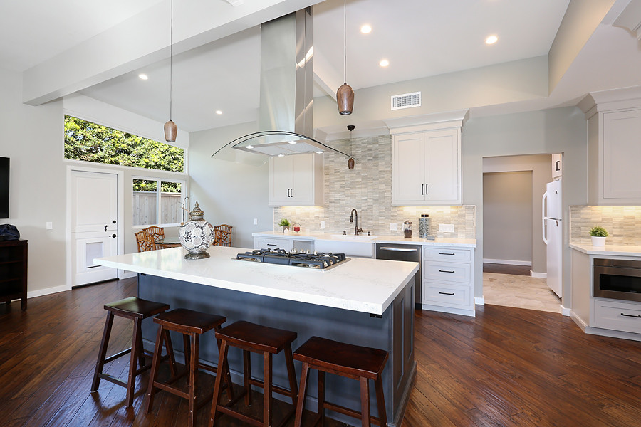 Example of a large transitional galley dark wood floor and brown floor open concept kitchen design in Orange County with a farmhouse sink, shaker cabinets, white cabinets, soapstone countertops, gray backsplash, stone tile backsplash, stainless steel appliances and an island