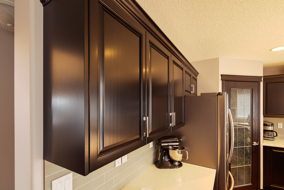 Eat-in kitchen - large transitional u-shaped dark wood floor and brown floor eat-in kitchen idea in Calgary with a double-bowl sink, raised-panel cabinets, dark wood cabinets, quartz countertops, gray backsplash, ceramic backsplash, stainless steel appliances and an island