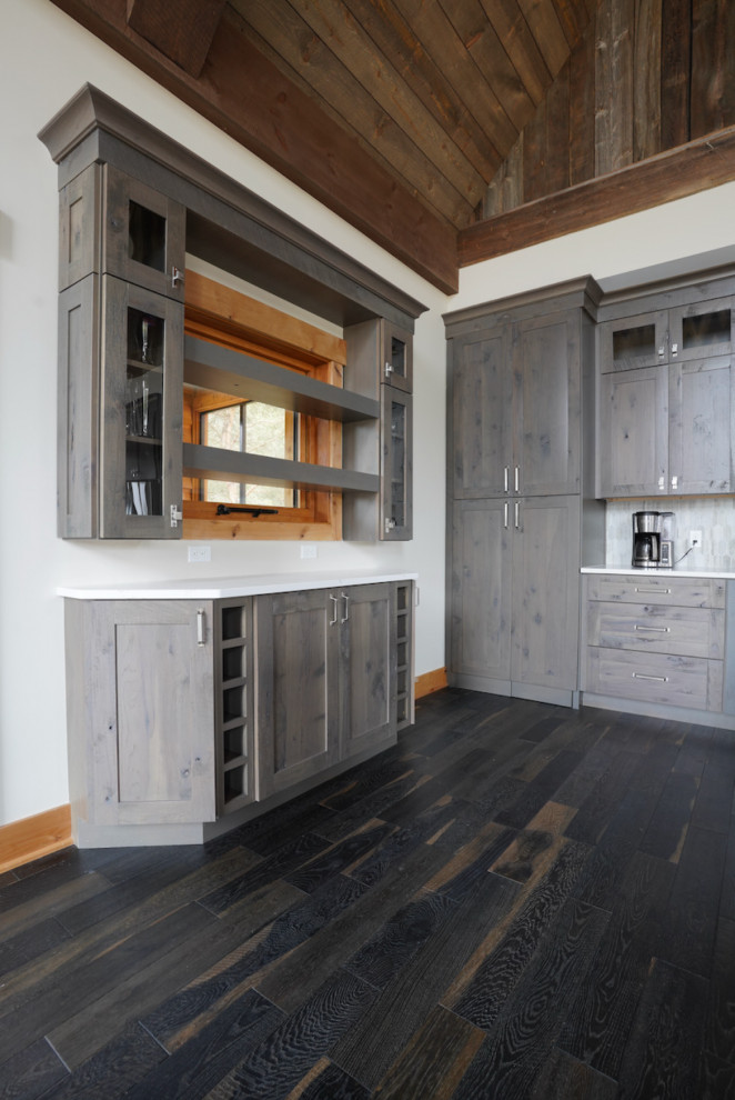 Example of a large mountain style l-shaped dark wood floor and brown floor open concept kitchen design with a drop-in sink, flat-panel cabinets, distressed cabinets, quartzite countertops, gray backsplash, ceramic backsplash, stainless steel appliances, an island and black countertops