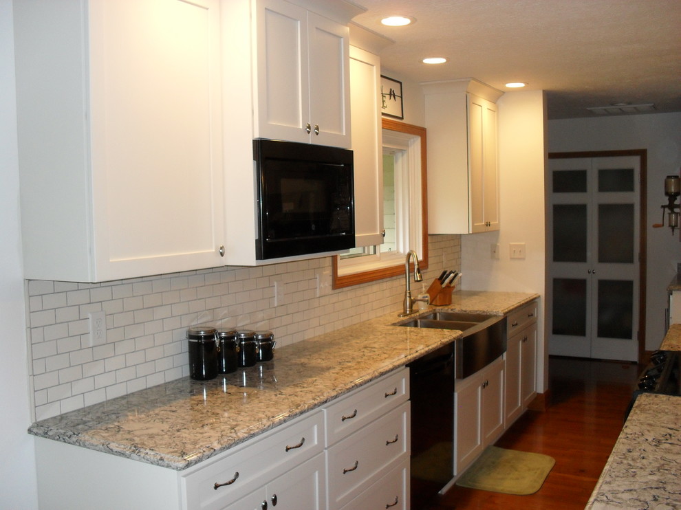 Example of a large transitional medium tone wood floor open concept kitchen design with white cabinets, white backsplash, black appliances, an island, a farmhouse sink and recessed-panel cabinets