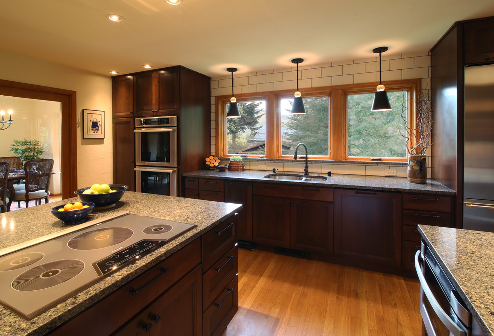 Transitional u-shaped light wood floor enclosed kitchen photo with an undermount sink, shaker cabinets, dark wood cabinets, quartz countertops, white backsplash, subway tile backsplash, stainless steel appliances and a peninsula