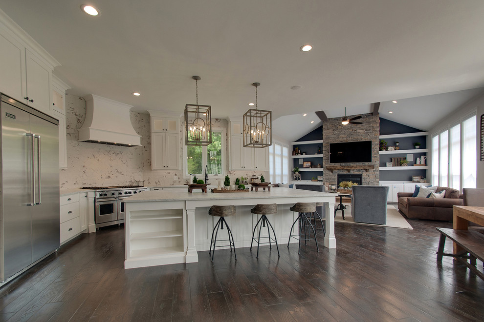 Photo of a large transitional l-shaped open plan kitchen in Nashville with a farmhouse sink, shaker cabinets, white cabinets, marble benchtops, white splashback, brick splashback, stainless steel appliances, dark hardwood floors, with island, brown floor and white benchtop.