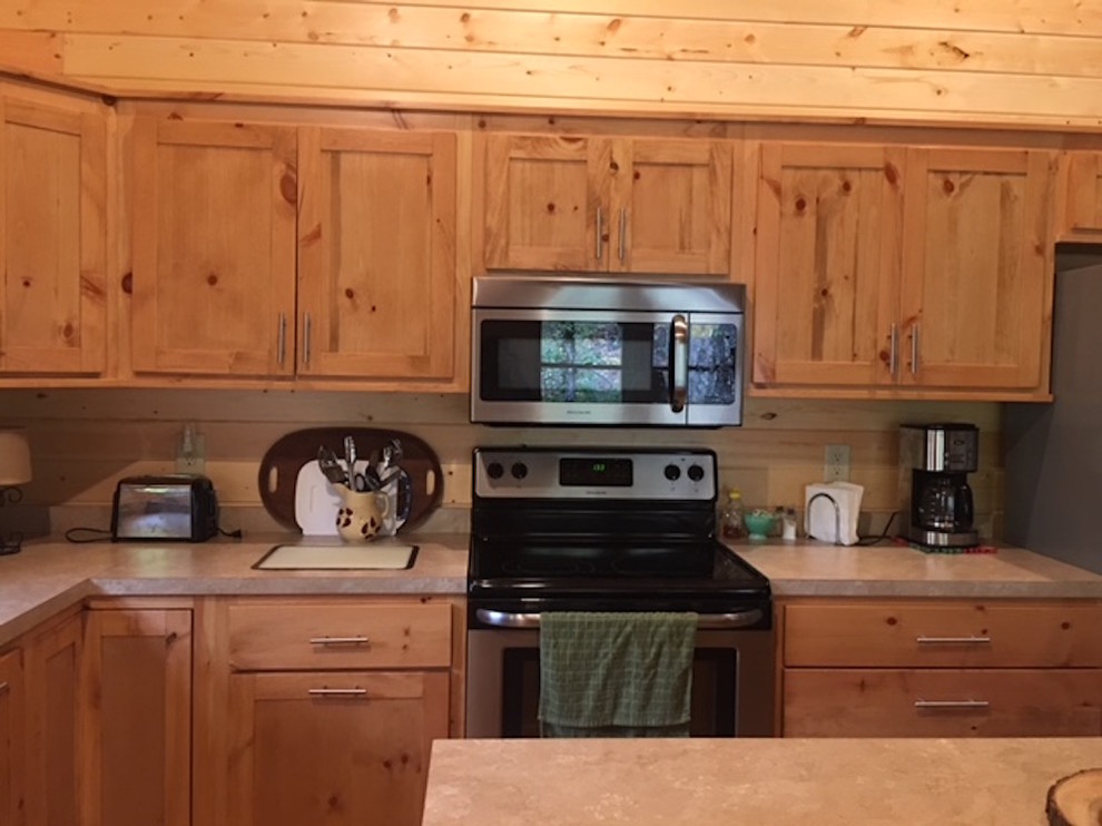 Example of a large mountain style l-shaped medium tone wood floor and brown floor kitchen design with a double-bowl sink, shaker cabinets, light wood cabinets, solid surface countertops, brown backsplash, wood backsplash and stainless steel appliances