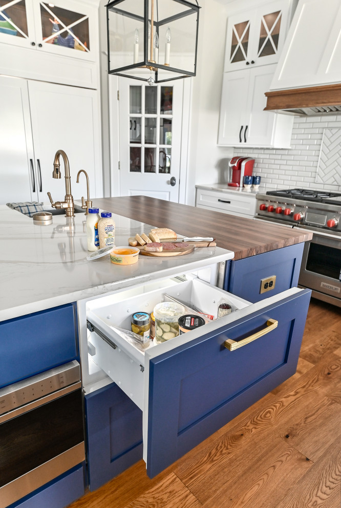 Design ideas for an expansive transitional u-shaped eat-in kitchen in Milwaukee with a farmhouse sink, shaker cabinets, blue cabinets, quartzite benchtops, white splashback, subway tile splashback, panelled appliances, vinyl floors, with island, brown floor and white benchtop.