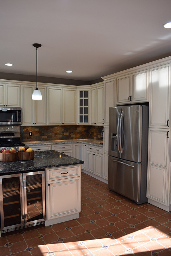 This is an example of a mid-sized traditional u-shaped eat-in kitchen in DC Metro with an undermount sink, raised-panel cabinets, white cabinets, granite benchtops, multi-coloured splashback, stone tile splashback, stainless steel appliances, terra-cotta floors, with island and red floor.