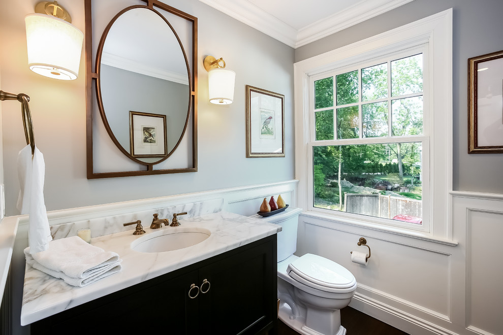 This is an example of a mid-sized transitional powder room in New York with shaker cabinets, grey cabinets, a two-piece toilet, blue walls, dark hardwood floors, an undermount sink and marble benchtops.