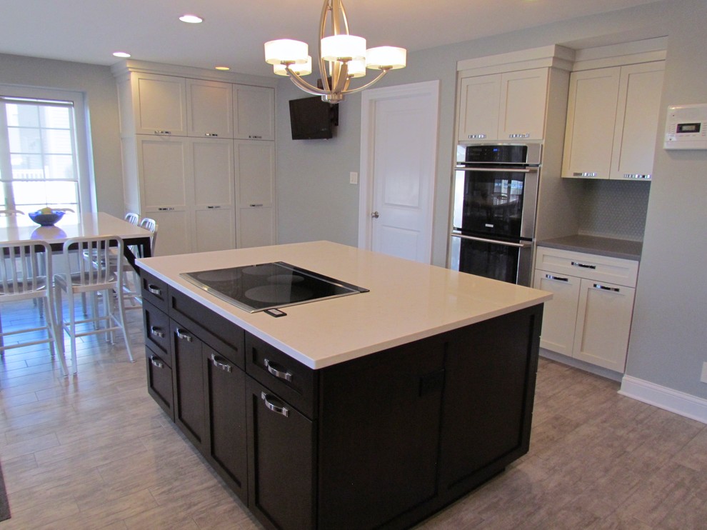 Example of a transitional l-shaped porcelain tile eat-in kitchen design in Chicago with a farmhouse sink, shaker cabinets, white cabinets, quartz countertops, blue backsplash, glass tile backsplash, stainless steel appliances and an island