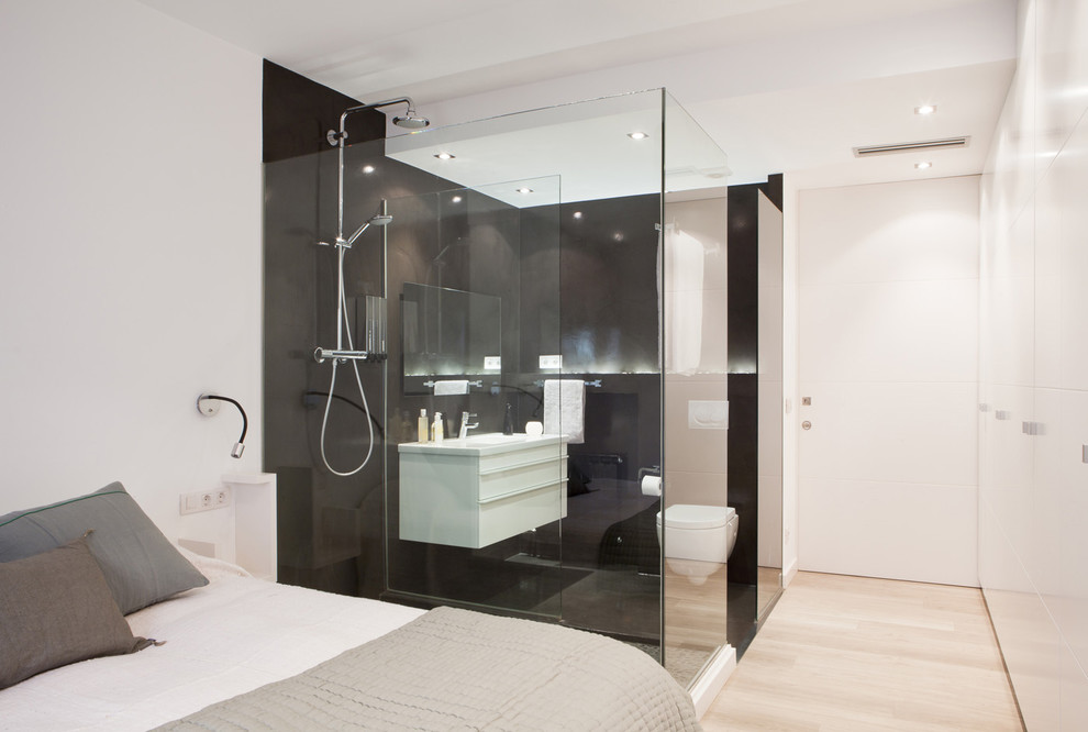 Design ideas for a mid-sized contemporary 3/4 bathroom in Barcelona with flat-panel cabinets, white cabinets, a wall-mount toilet, black tile, black walls, an integrated sink, a curbless shower and light hardwood floors.