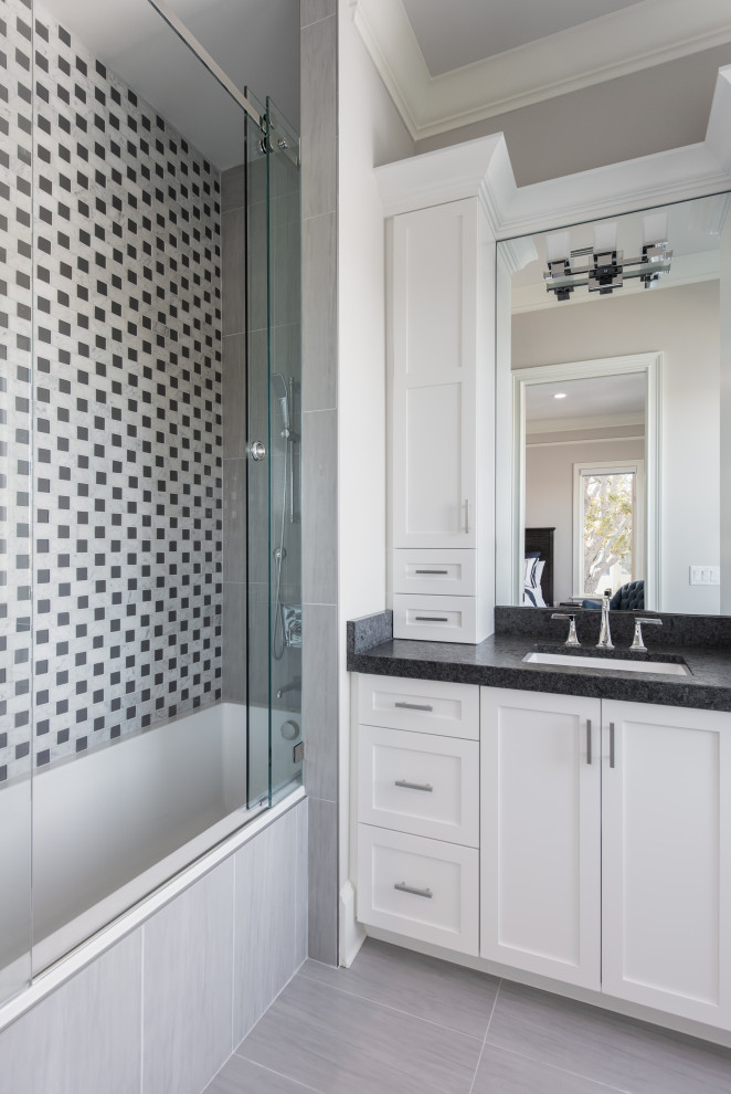 This is an example of a mid-sized transitional kids bathroom in Tampa with recessed-panel cabinets, white cabinets, an alcove tub, a shower/bathtub combo, black and white tile, beige walls, an undermount sink, a sliding shower screen, black benchtops, a single vanity and a built-in vanity.