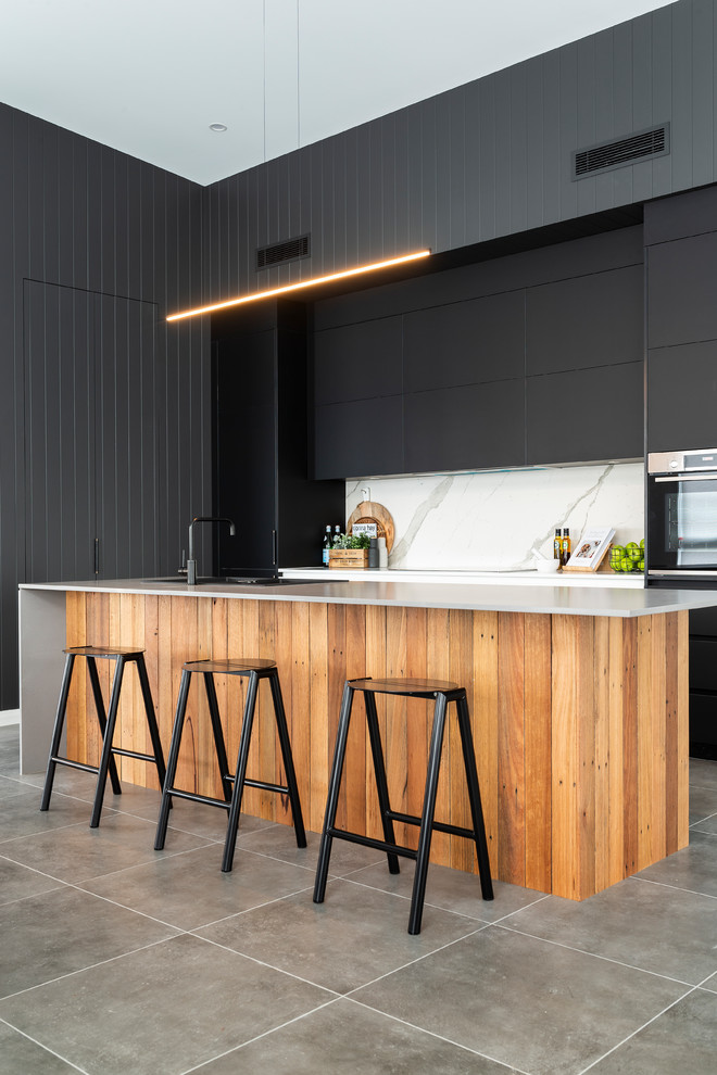 Photo of a large contemporary l-shaped kitchen in Canberra - Queanbeyan with black cabinets, quartz benchtops, white splashback, porcelain splashback, black appliances, porcelain floors, grey floor, a drop-in sink, flat-panel cabinets and with island.