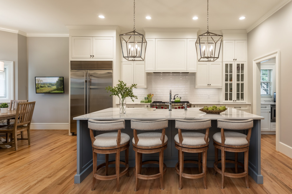 Example of a mid-sized transitional single-wall medium tone wood floor and brown floor open concept kitchen design with a farmhouse sink, recessed-panel cabinets, white cabinets, marble countertops, white backsplash, cement tile backsplash, stainless steel appliances, an island and white countertops