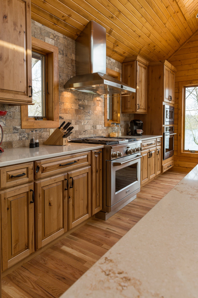 This is an example of a country open plan kitchen in Milwaukee with an undermount sink, raised-panel cabinets, medium wood cabinets, quartzite benchtops, stainless steel appliances, light hardwood floors and with island.