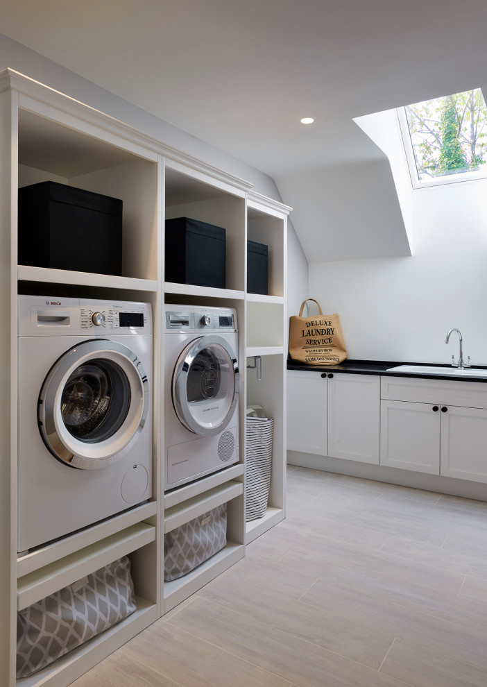 Large beach style laundry room in Hertfordshire with quartzite benchtops, grey floor and black benchtop.