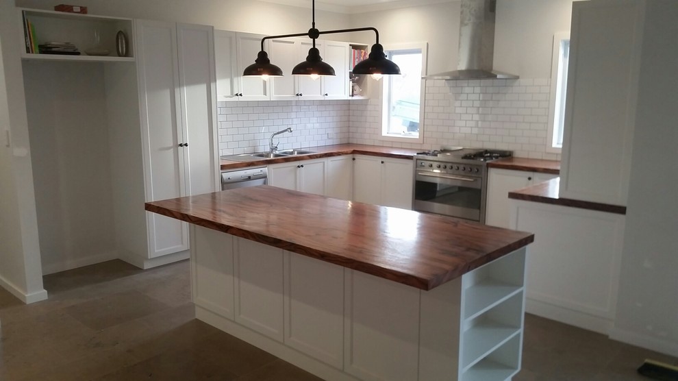 Inspiration for a mid-sized traditional u-shaped eat-in kitchen in Perth with a double-bowl sink, recessed-panel cabinets, white cabinets, wood benchtops, white splashback, ceramic splashback, stainless steel appliances, ceramic floors and with island.
