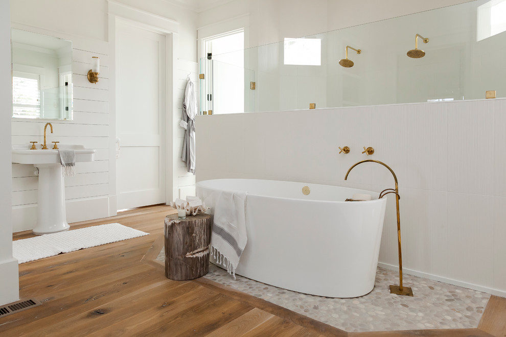 Design ideas for a beach style master bathroom in Charleston with a pedestal sink, a freestanding tub, a double shower, white walls and medium hardwood floors.