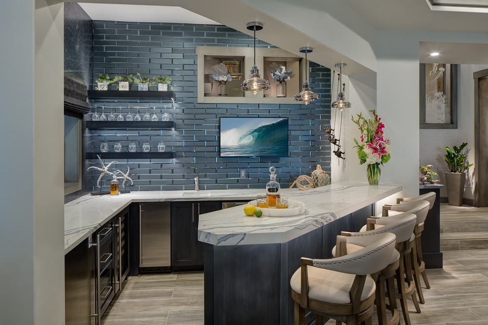 Inspiration for a mid-sized beach style u-shaped seated home bar in Orange County with an undermount sink, shaker cabinets, blue cabinets, quartz benchtops, blue splashback, porcelain floors, multi-coloured benchtop, subway tile splashback and beige floor.