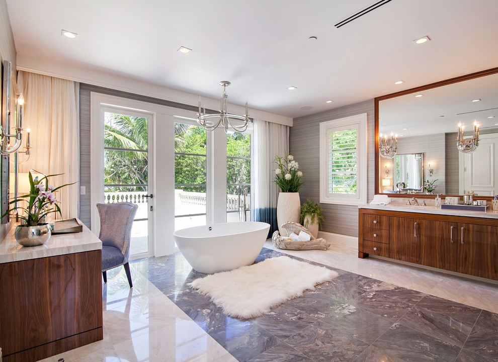 Example of a huge transitional master gray tile and stone slab marble floor freestanding bathtub design in Miami with flat-panel cabinets, medium tone wood cabinets, gray walls and marble countertops