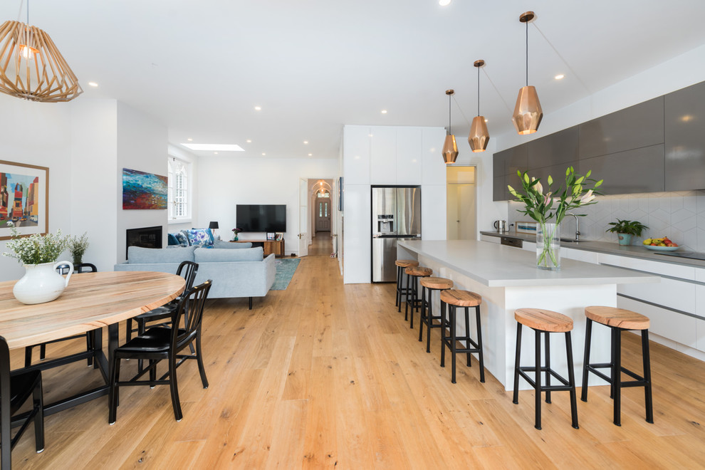 Inspiration for a large contemporary l-shaped open plan kitchen in Melbourne with an undermount sink, flat-panel cabinets, white cabinets, white splashback, stainless steel appliances, medium hardwood floors, with island and brown floor.