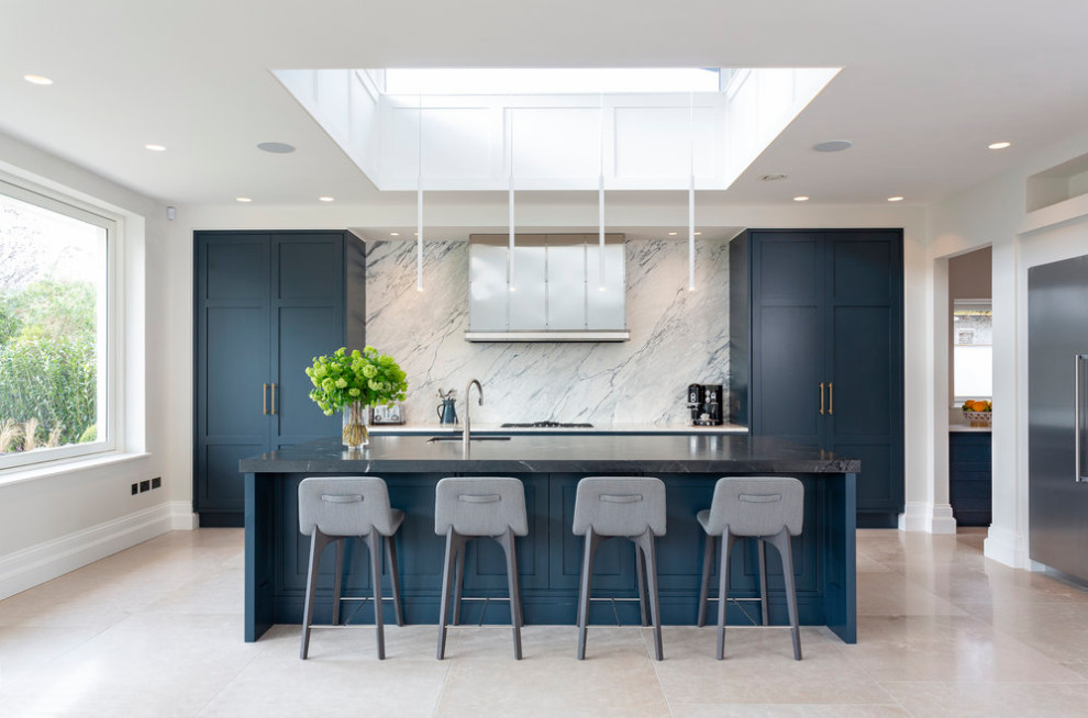This is an example of a large contemporary galley kitchen in Dublin with an undermount sink, shaker cabinets, blue cabinets, grey splashback, stainless steel appliances, porcelain floors, with island, beige floor and black benchtop.