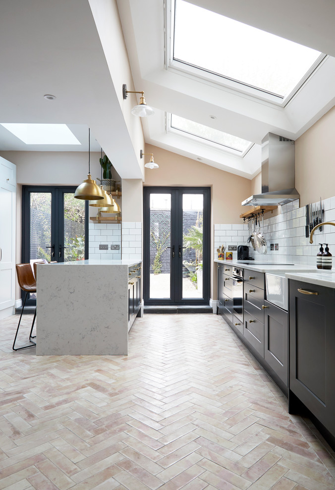 Design ideas for a mid-sized modern open plan kitchen in London with a farmhouse sink, flat-panel cabinets, grey cabinets, solid surface benchtops, white splashback, ceramic splashback, stainless steel appliances, ceramic floors, with island, orange floor and white benchtop.