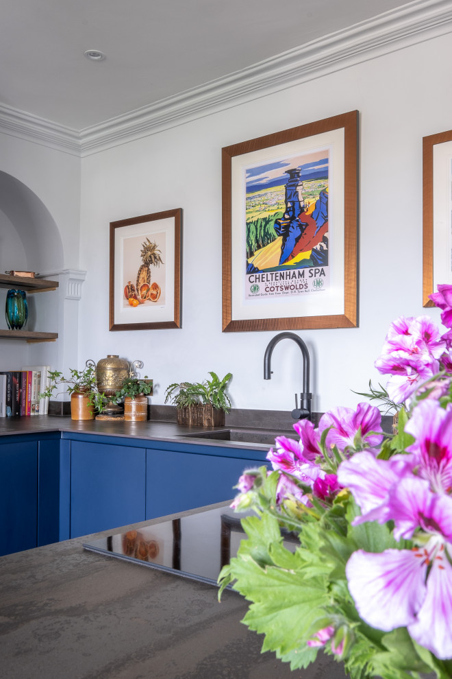 Photo of a small bohemian u-shaped enclosed kitchen in Gloucestershire with a built-in sink, flat-panel cabinets, blue cabinets, composite countertops, black appliances and grey worktops.