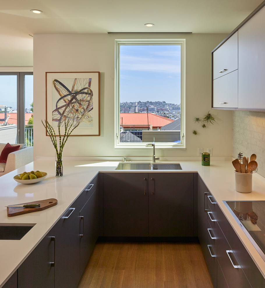 Photo of a small contemporary u-shaped open plan kitchen in San Francisco with flat-panel cabinets, medium hardwood floors, a peninsula, a double-bowl sink, blue cabinets, quartzite benchtops, grey splashback and stone tile splashback.