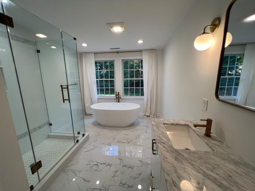 Inspiration for a medium sized contemporary bathroom in New York with a freestanding bath, a corner shower, a one-piece toilet, white tiles, ceramic tiles, white walls, porcelain flooring, a submerged sink, marble worktops, white floors, a hinged door, a wall niche and double sinks.