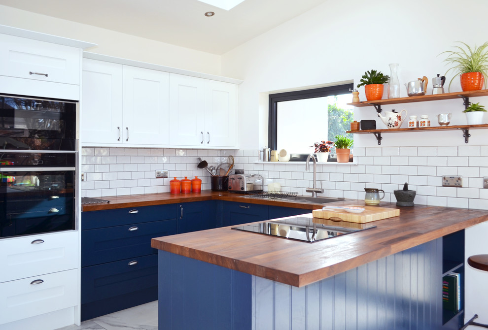 This is an example of a mid-sized transitional u-shaped eat-in kitchen in Edinburgh with shaker cabinets, blue cabinets, wood benchtops, a peninsula, a drop-in sink, white splashback, subway tile splashback and white floor.
