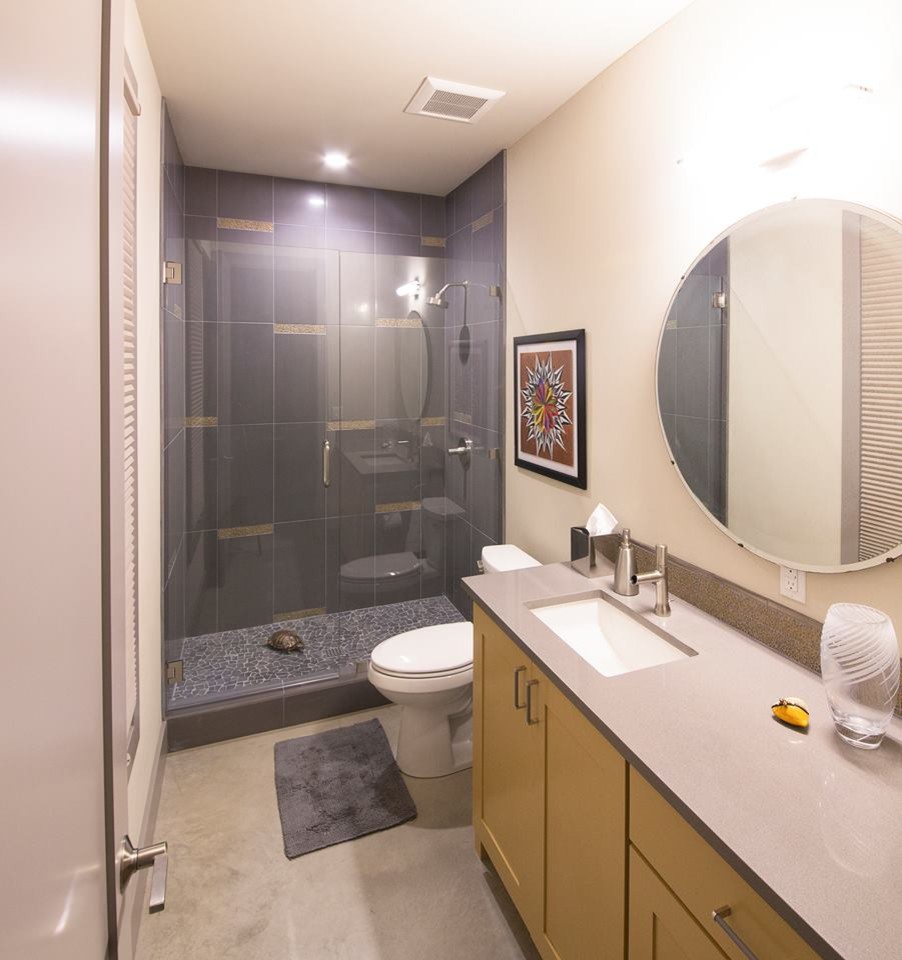 Alcove shower - mid-sized transitional 3/4 gray tile concrete floor and gray floor alcove shower idea in Austin with shaker cabinets, yellow cabinets, a two-piece toilet, beige walls, an undermount sink, quartz countertops, a hinged shower door and gray countertops