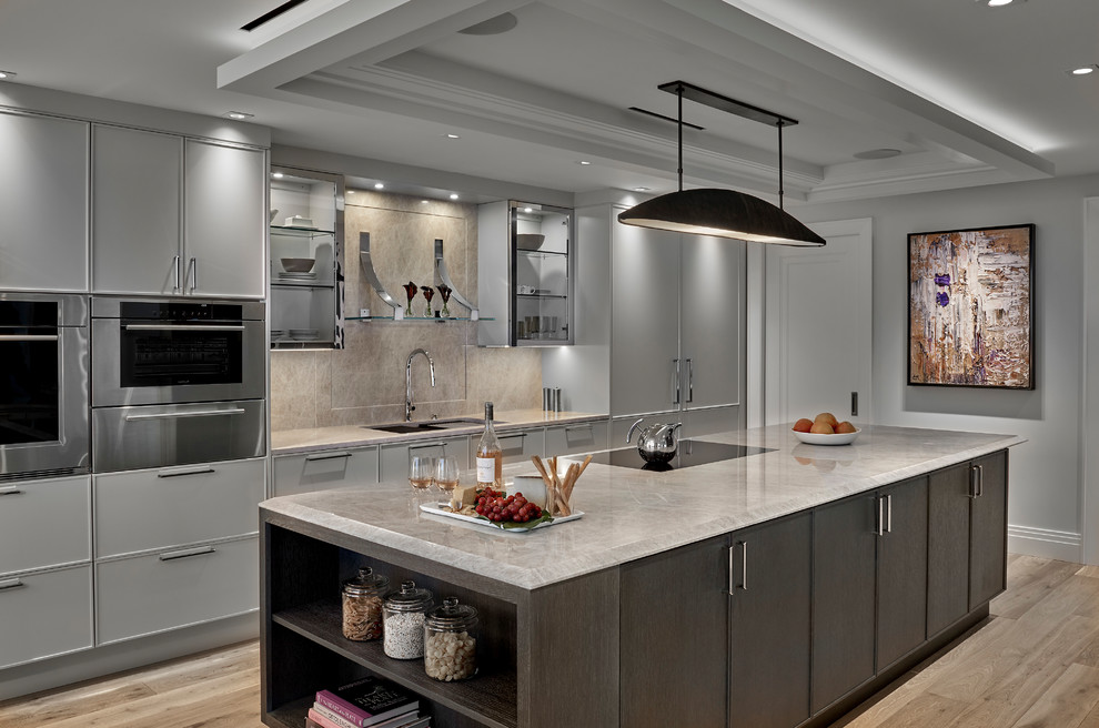 This is an example of a contemporary galley kitchen in Chicago with an undermount sink, flat-panel cabinets, grey cabinets, beige splashback, stone slab splashback, panelled appliances, light hardwood floors, with island, beige floor and beige benchtop.