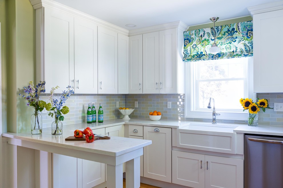 Small transitional u-shaped kitchen in Boston with a farmhouse sink, stainless steel appliances, medium hardwood floors, white benchtop, shaker cabinets, white cabinets, multi-coloured splashback, subway tile splashback, a peninsula and brown floor.