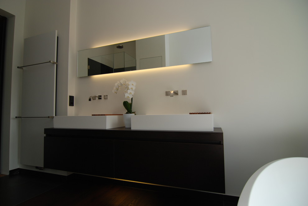 Großes Modernes Badezimmer mit Aufsatzwaschbecken, Waschtisch aus Holz, freistehender Badewanne, bodengleicher Dusche, Wandtoilette, grauen Fliesen, Steinfliesen und weißer Wandfarbe in Düsseldorf