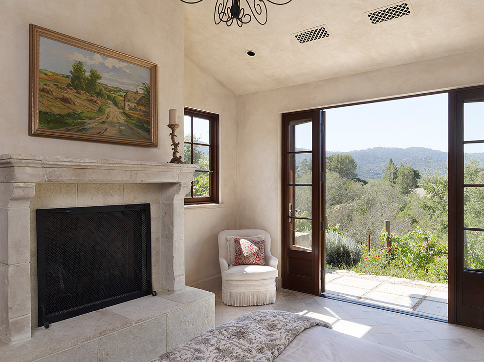 Photo of a mid-sized mediterranean guest bedroom in San Francisco with a standard fireplace, beige walls, limestone floors and a stone fireplace surround.