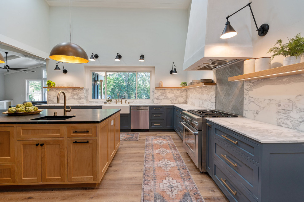 This is an example of a transitional u-shaped eat-in kitchen in San Francisco with a farmhouse sink, shaker cabinets, blue cabinets, marble benchtops, multi-coloured splashback, marble splashback, stainless steel appliances, medium hardwood floors, with island, brown floor and multi-coloured benchtop.