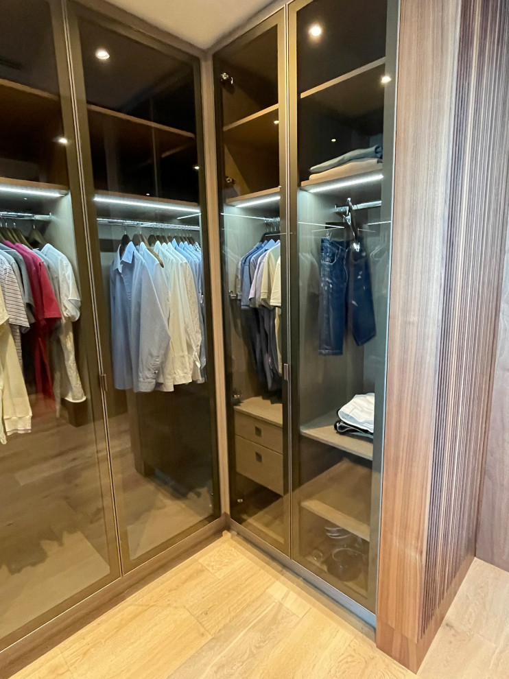 Inspiration for a mid-sized transitional gender-neutral dressing room in Miami with glass-front cabinets, medium wood cabinets, medium hardwood floors, beige floor and wood.