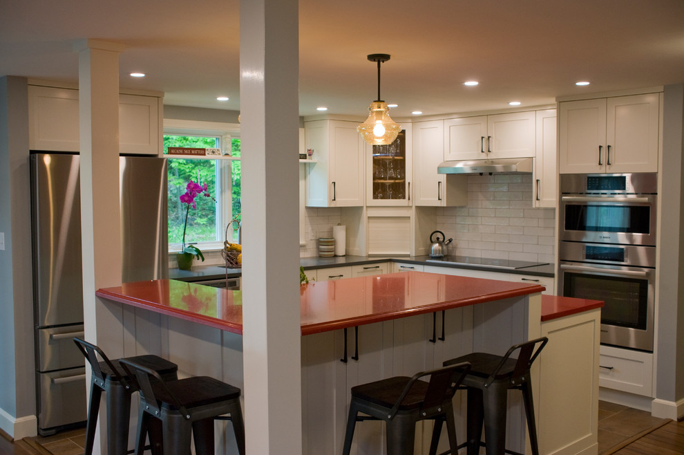 Mid-sized eclectic l-shaped eat-in kitchen in Boston with an undermount sink, recessed-panel cabinets, white cabinets, quartz benchtops, white splashback, subway tile splashback, stainless steel appliances, porcelain floors, with island, brown floor and red benchtop.