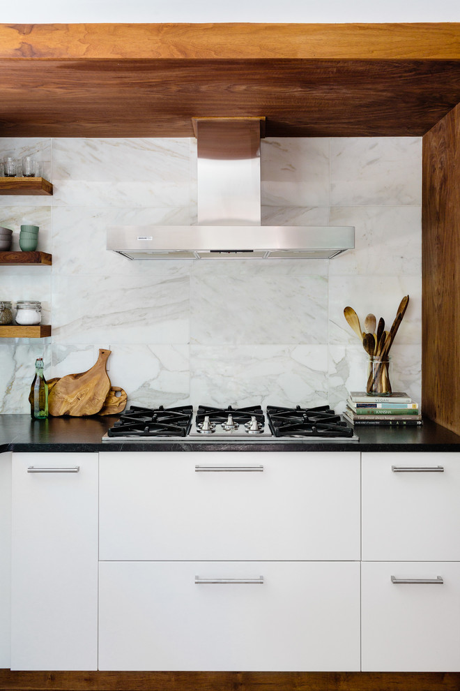 Photo of a small contemporary kitchen in Boston with flat-panel cabinets, white cabinets, soapstone benchtops, white splashback, stone tile splashback, stainless steel appliances and light hardwood floors.