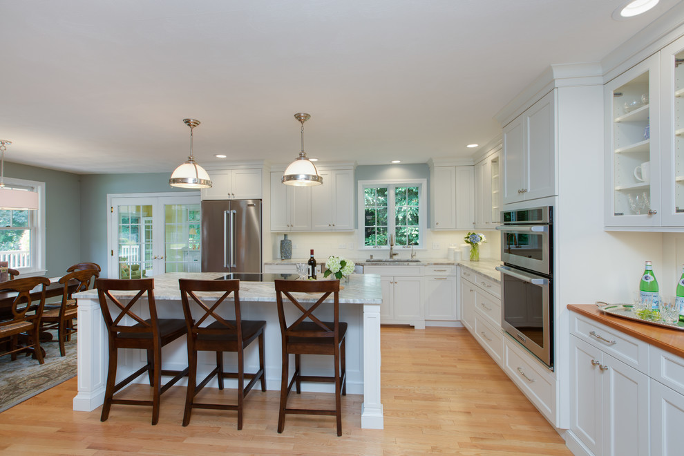 Example of a transitional l-shaped light wood floor eat-in kitchen design in Boston with an undermount sink, recessed-panel cabinets, white cabinets, quartzite countertops, white backsplash, subway tile backsplash, stainless steel appliances and an island