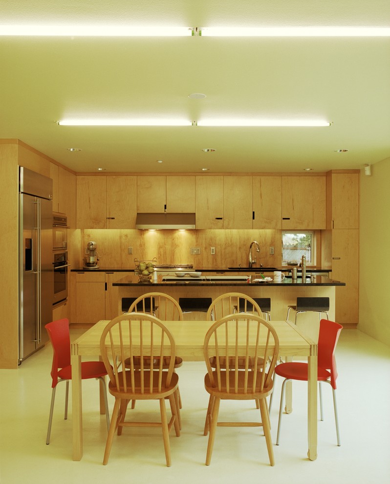 Design ideas for a mid-sized modern l-shaped eat-in kitchen in Seattle with a double-bowl sink, flat-panel cabinets, light wood cabinets, granite benchtops, stainless steel appliances, concrete floors, with island, green floor and black benchtop.